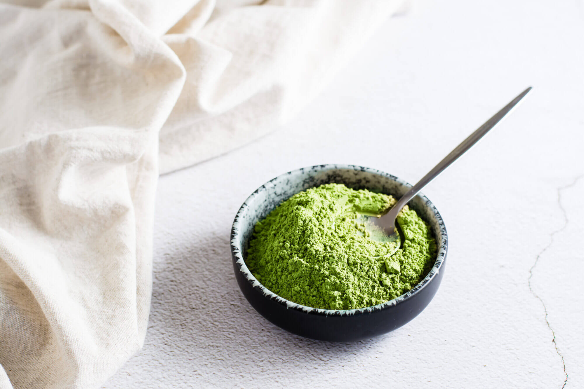 Organic green matcha tea powder in bowl and spoon on table