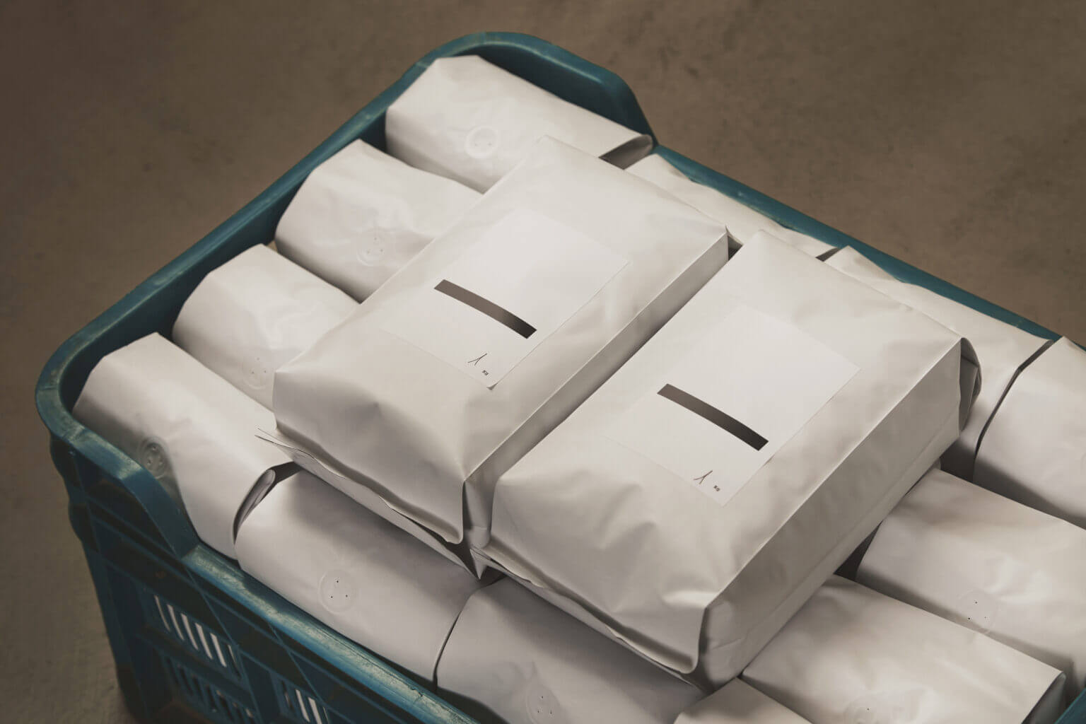 Closeup white filled with coffee or tea kg sealed packages in plastic box on concrete floor in warehouse. Two packages on top with blank labels. Ready to ship for sale. Small artisan business concept